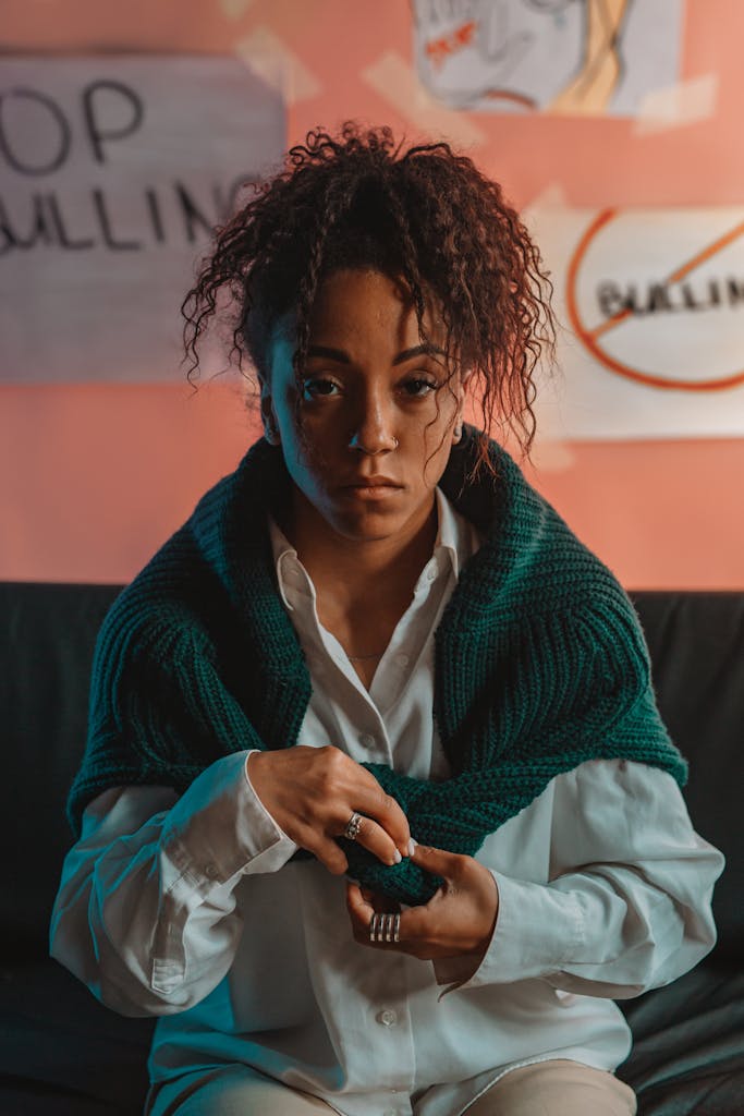 Young woman in a thoughtful pose, sitting in anti-bullying themed room with posters.